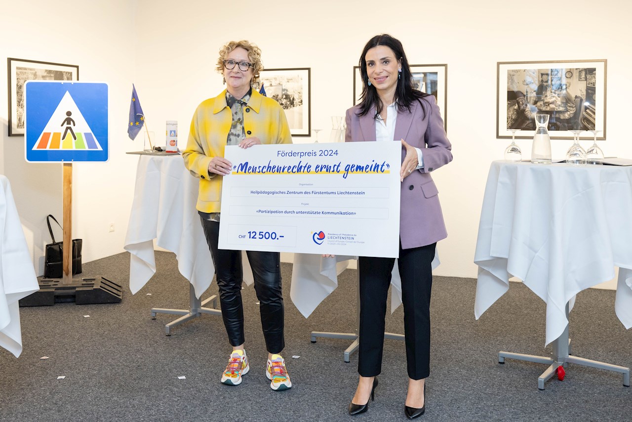 Regierungsrätin Dominique Hasler posiert mit einer Vertreterin des Heilpädagogischen Zentrums Liechtenstein. Gemeinsam halten sie den Siegerscheck für das Projekt Partizipation durch unterstützte Kommunikation.