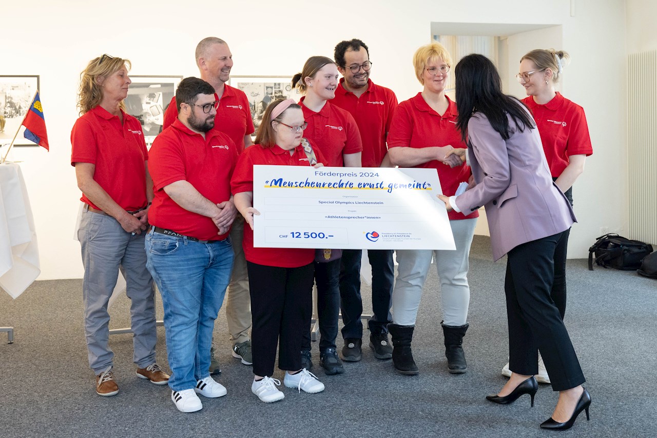 Regierungsrätin Dominique Hasler gratuliert dem Team des Projekts Athletensprecher/innen von Special Olympics Liechtenstein und überreicht ihnen den Siegerscheck.