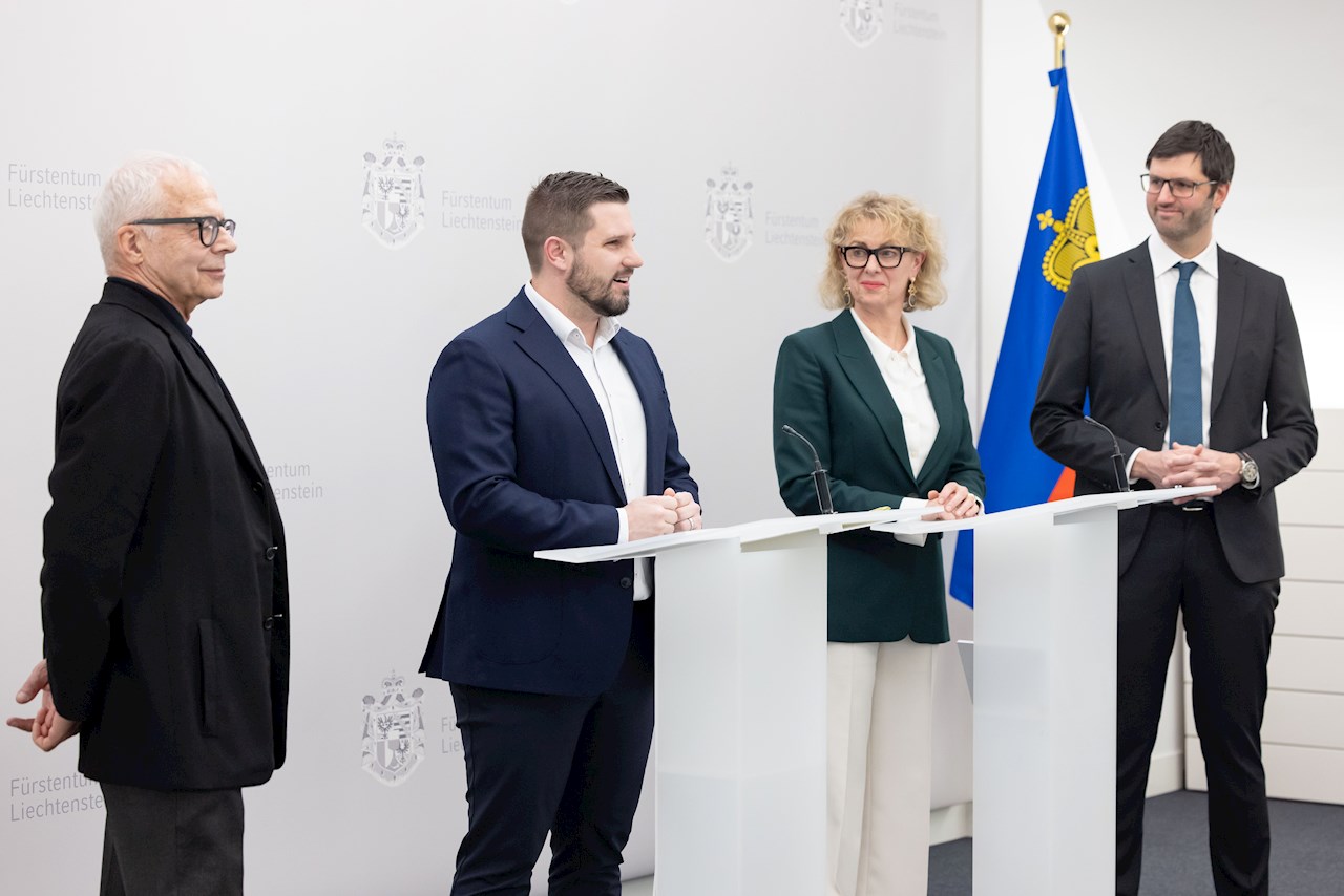 Peter Goop, Florian Meier, Graziella Marok-Wachter und Pascal Seger stehen vor Fotowand im Medienraum, Florian Meier spricht am Rednerpult